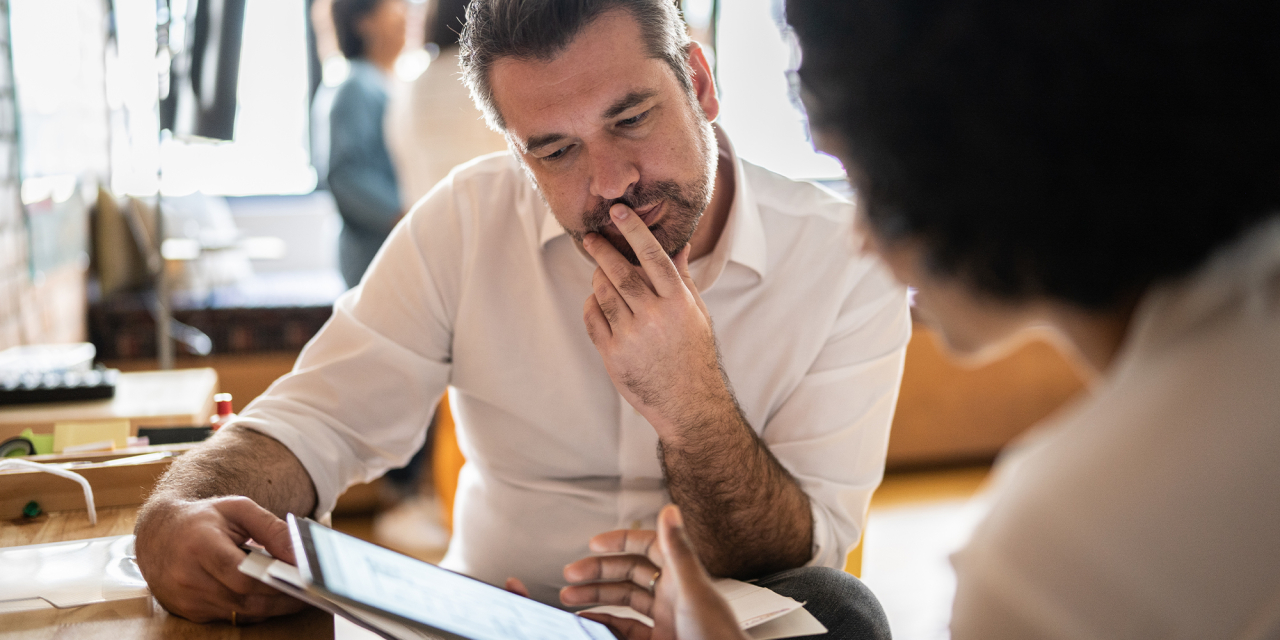Two people sat at a desk discussing items on paper and a tablet computer.